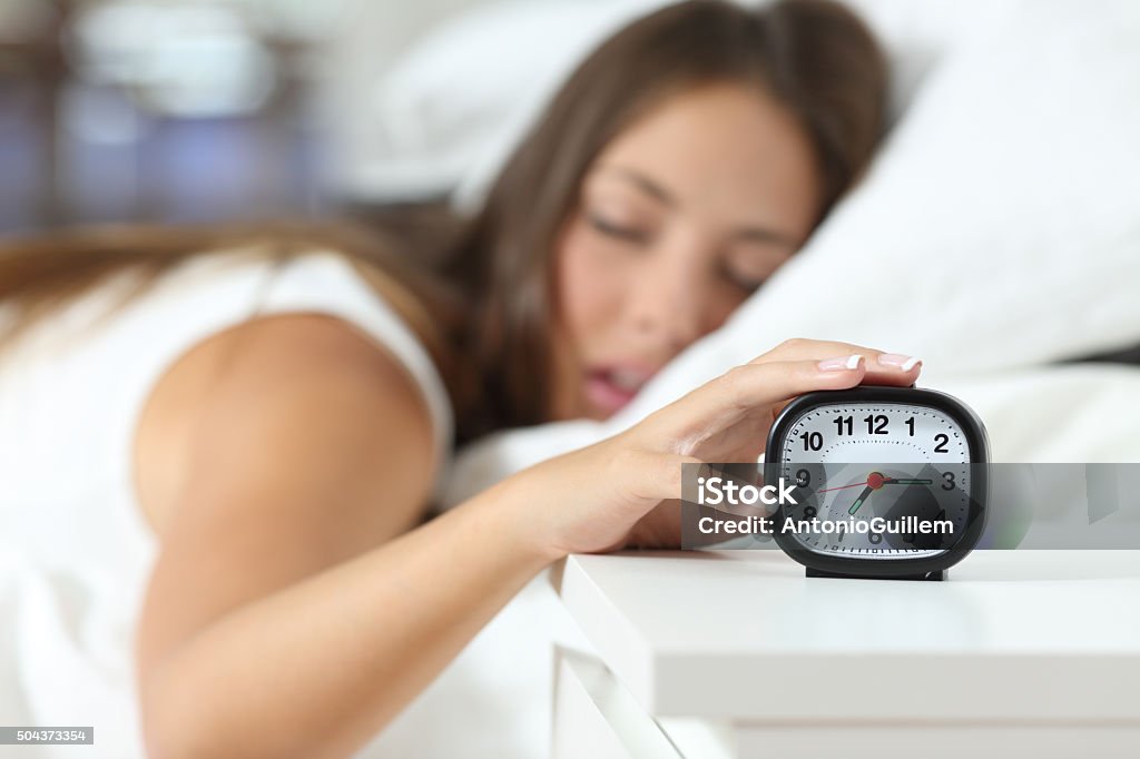 Wake up of an asleep girl stopping alarm clock Wake up of an asleep girl stopping alarm clock on the bed in the morning Waking up Stock Photo