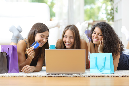 Three friends shopping online with credit card and laptop lying on the floor at home
