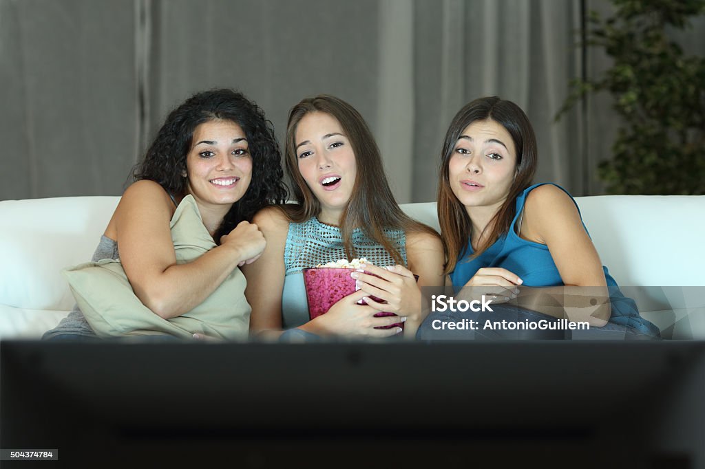 Three friends watching romantic movie on tv Three friends watching romantic movie on tv sitting on a couch at home Television Industry Stock Photo