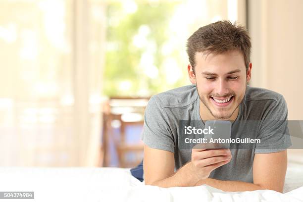 Guy Using A Mobile Phone On A Bed At Home Stock Photo - Download Image Now - Adult, Asking, Beautiful People