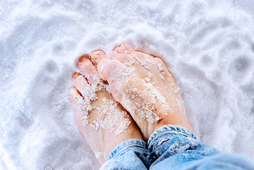 Close up of bare feet getting really cold on ice and snow during winter.