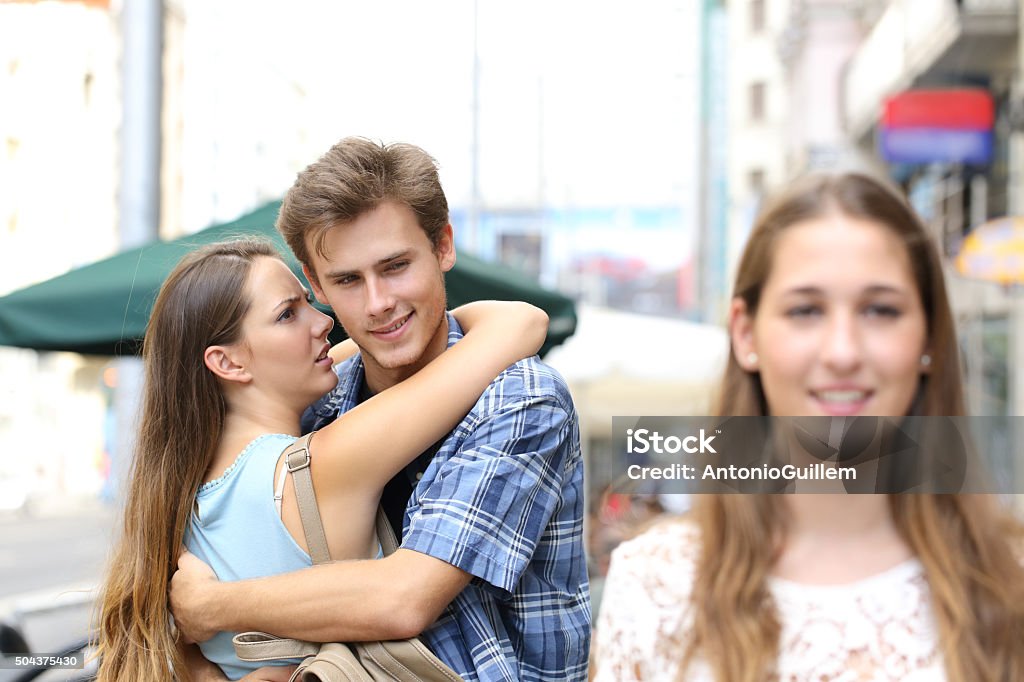 Unfaithful man hugging his girlfriend and looking another Unfaithful man hugging his girlfriend while is looking another one in the street Envy Stock Photo