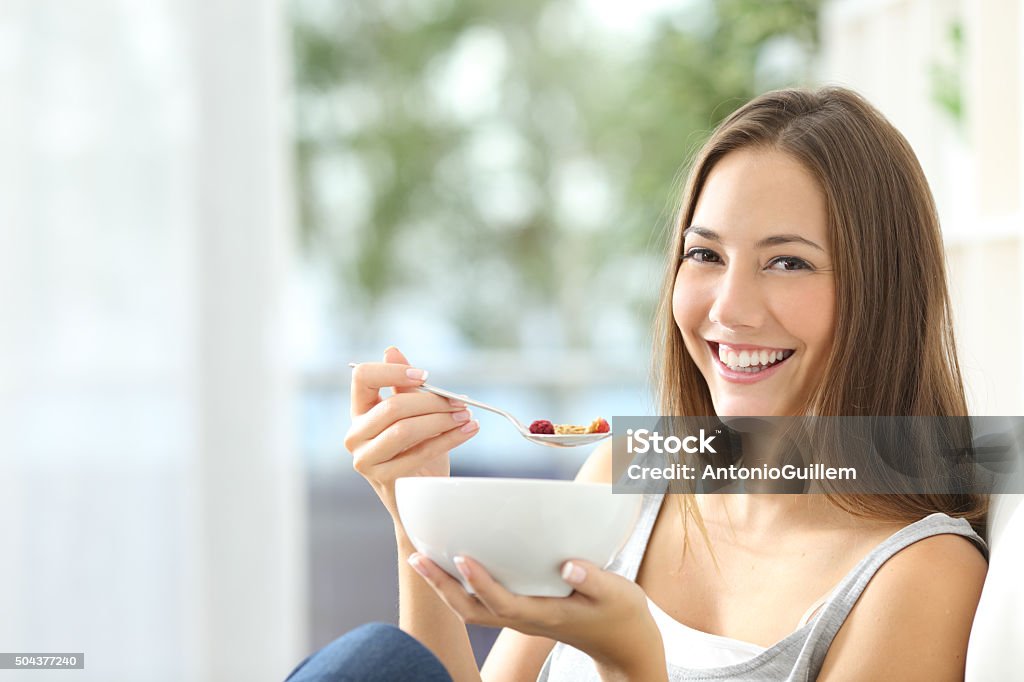 Woman eating cornflakes at home Casual happy woman dieting and eating cornflakes sitting on a couch at home Breakfast Cereal Stock Photo