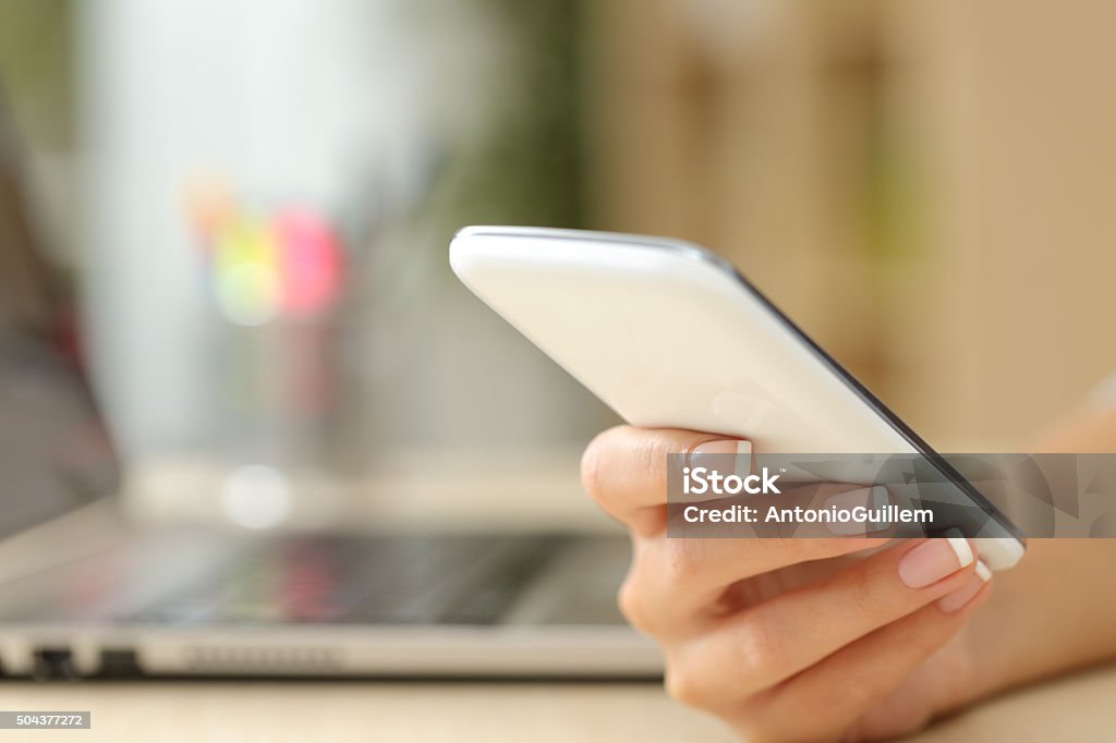 Woman hand using a white smart phone Close up of a woman hand using a white smart phone on a desk at home Adult Stock Photo