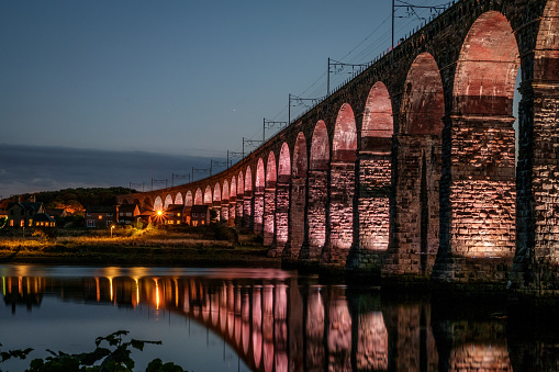 Illuminated Royal Border Bridge (Berwick Viaduct) over the River Tweed between Berwick-upon-Tweed and Tweedmouth in Northumberland, England. The railway viaduct, built between 1847 and 1850, is 659 metres (2,162 ft) long, has 28 arches, each spanning 60 feet (18 m). The railway is carried 37 metres (121 ft) above the river level.