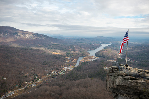 Chimney Rock, North Carolina, USA - December 7, 2012: A visitor stands beneath an American flag on Chimney Rock in Chimney Rock State Park, North Carolina. Lake Lure is below.