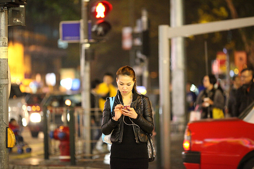 Hong Kong, Hong Kong - January 12, 2013: A young woman checks her smartphone at an intersection in Hong Kong. 