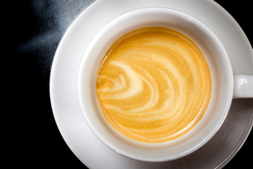 Espresso shot patterns in a cappucino cup on a black granite surface.