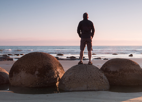 Man stands on a boulder at ocean shore