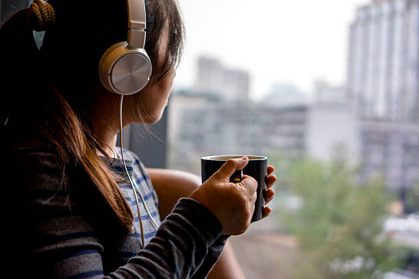 istock girl wearing earphone,drinking coffee beside window 504424478