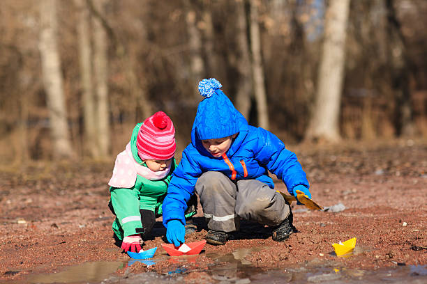 kleine jungen und mädchen spielen mit wasser im frühling - puddle rain boot water stock-fotos und bilder