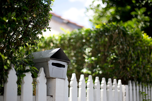 Mailbox attached to a picket fence with hedge in background.