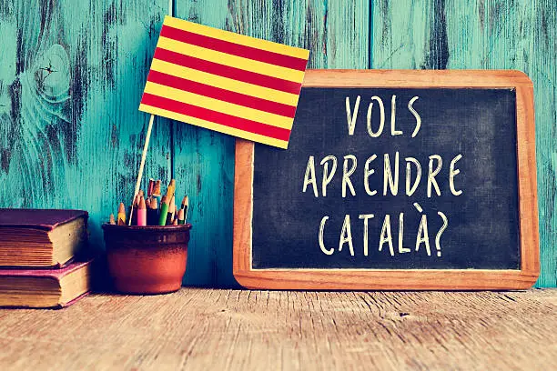 a flag of Catalonia and a chalkboard with the question vols aprendre catala?, do you want to learn Catalan? written in Catalan in it