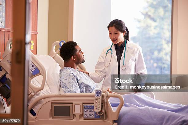 Female Doctor Talking To Male Patient In Hospital Bed Stock Photo - Download Image Now
