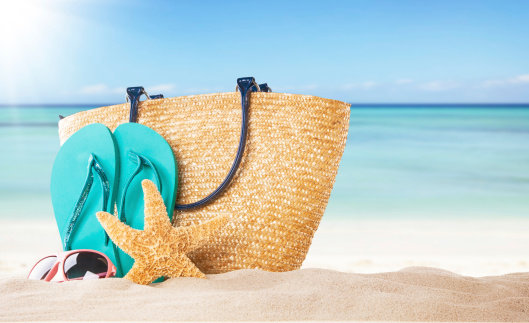 Summer concept with sandy beach, shells and blue sandals