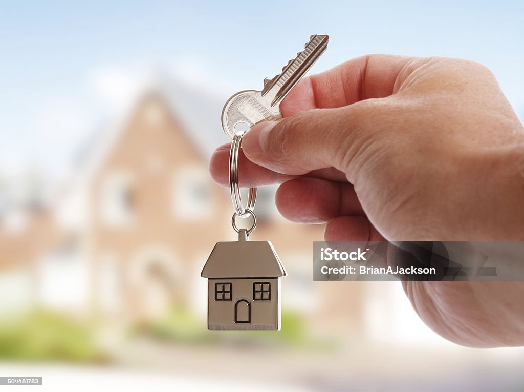 Giving house keys Holding house keys on house shaped keychain in front of a new home Key Stock Photo