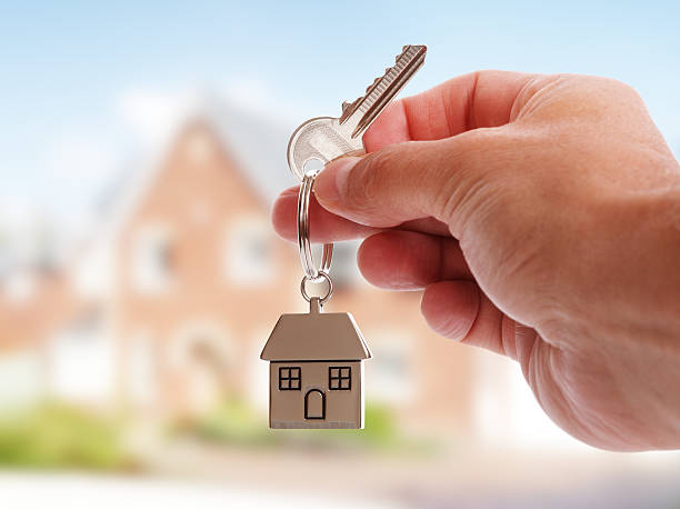Giving house keys Holding house keys on house shaped keychain in front of a new home house key photos stock pictures, royalty-free photos & images