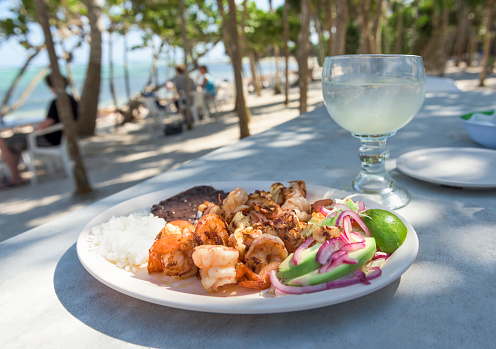 A fresh platter of shrimp, grilled with garlic and butter with rice, beans, and avocado - on a beach covered with Palm Trees on Soliman Bay near Tulum, Mexico
