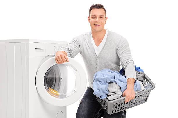 Content young man doing laundry Content young man holding a laundry basket and standing next to a washing machine isolated on white background laundry husband housework men stock pictures, royalty-free photos & images