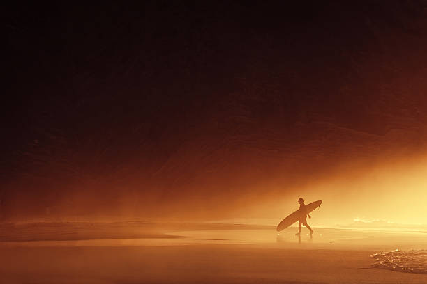 surfer silhouette at misty sunset surfer silhouette exiting water at misty sunset sopelana stock pictures, royalty-free photos & images