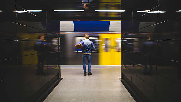 Waiting for the Train Rear view of a young, hipster styled, man standing waiting for a train. The train can be seen moving in front of him past the station in a blur. standing on subway platform stock pictures, royalty-free photos & images