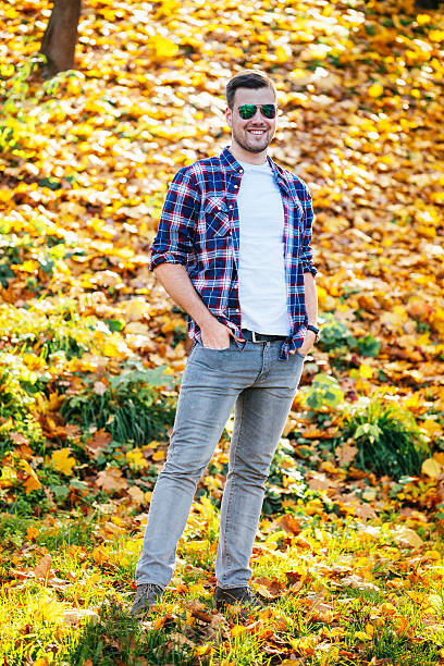 Portrait of young handsome caucasian man in plaid shirt and jeans walking down the pathway in park or forest in sunny autumn afternoon. Camer hidden behind the leaves. Image taken with Nikon D800 and 70-200 pro lens, developed from RAW.Location: Novi Sad, Serbia, Europe