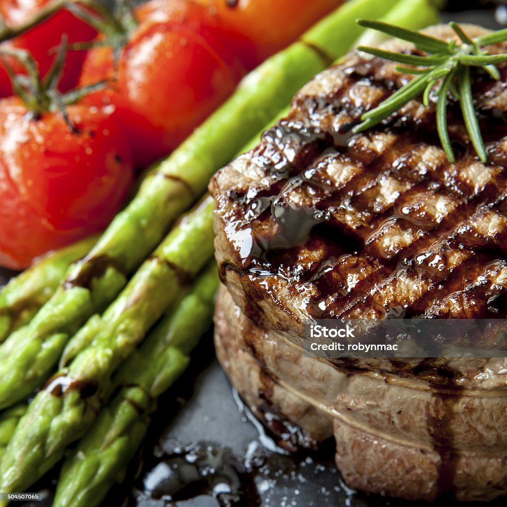 Filet Mignon with Asparagus and Cherry Tomatoes Filet mignon grilled beef steak, with asparagus and cherry tomatoes.  Isolated on white.Filet mignon grilled beef steak, with asparagus and cherry tomatoes.  On black plate. Asparagus Stock Photo