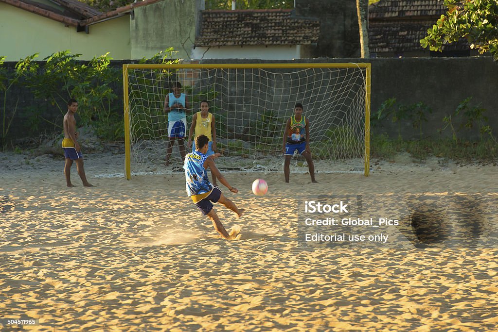 Soccer Players Alcobaça, Brazil - July, 03 2014: Local young boys are playing soccer on a sand field at their neighborhood just before the sun goes down at Alcobaça city, Bahia state. Community Stock Photo