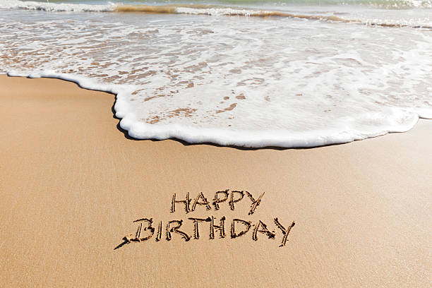 Buon compleanno scritto nella sabbia su una spiaggia. - foto stock