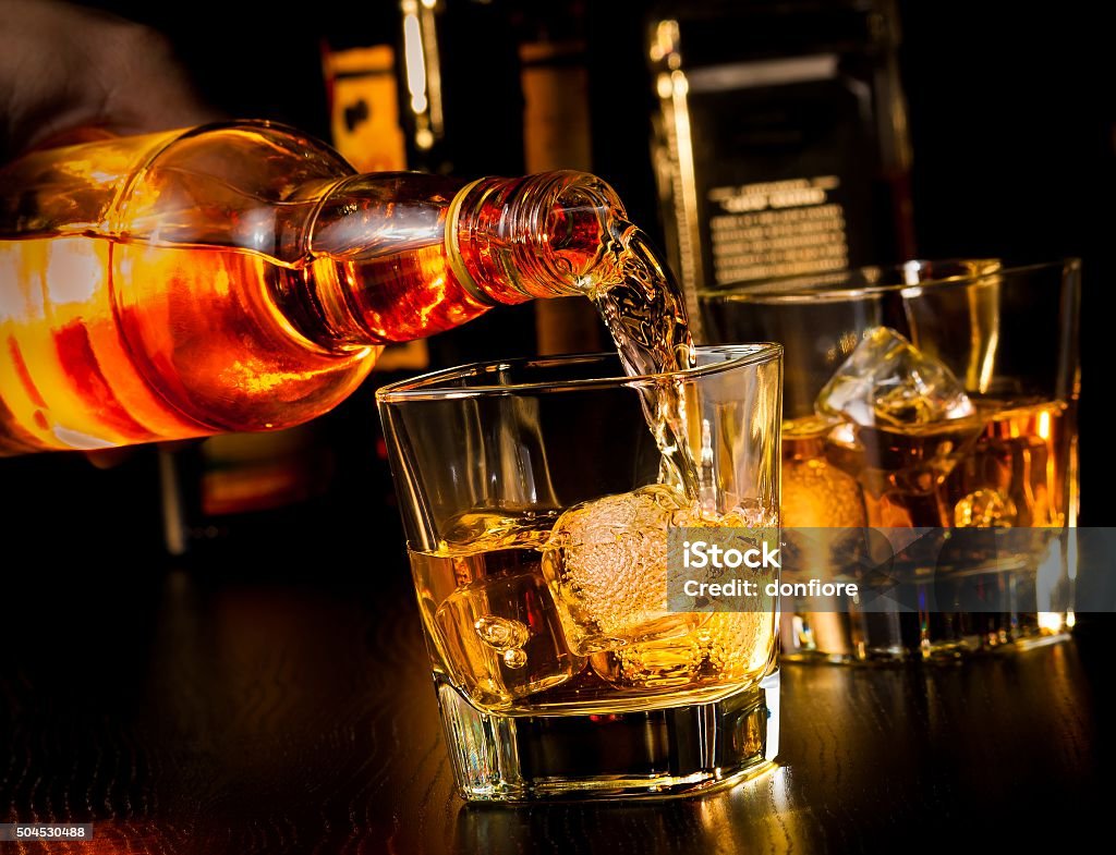 barman pouring whiskey in front of whiskey glass and bottles barman pouring whiskey in front of whiskey glass and bottles on wood table Bottle Stock Photo