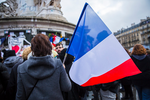Paris, France - January 10, 2016: woman in the crowd holding French flag during the ceremony Place de la Republique to commemorate victims of the bombing and shooting rampage, Charlie Hebdo terrorist attack and \