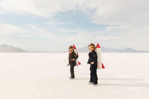 Two young business boys dressed in business suits wearing rockets and aviator goggles are ready to launch their business into the sky. The boys are standing on the Bonneville Salt Flats in Utah, USA.