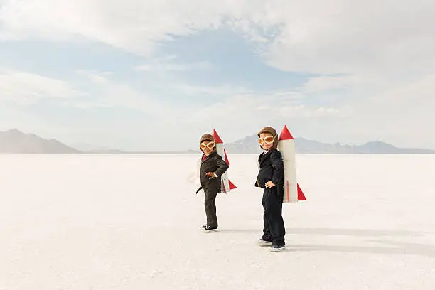 Two young business boys dressed in business suits wearing rockets and aviator goggles are ready to launch their business into the sky. The boys are standing on the Bonneville Salt Flats in Utah, USA.