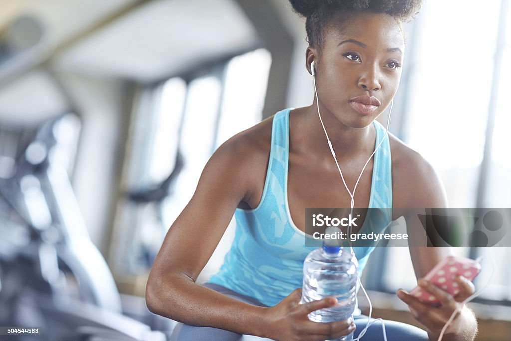 Getting into the zone Shot of a beautiful young woman listening to music and taking a water break at the gym Activity Stock Photo