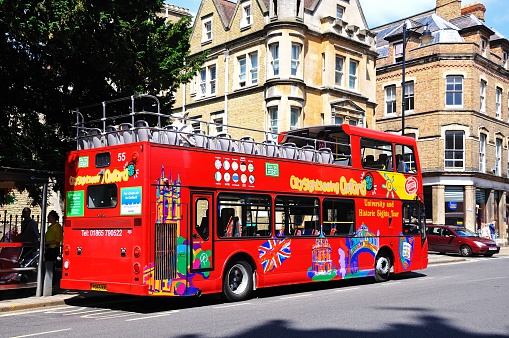Oxford, United Kingdom - June 17, 2014:  Red open topped Oxford tour bus carrying passengers travelling along St Aldates, Oxford, Oxfordshire, England, UK, Western Europe.