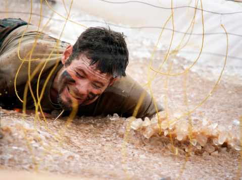 A man is submerged in mud and ice while going under the electric shock tentacles at a mud run obstacle course event