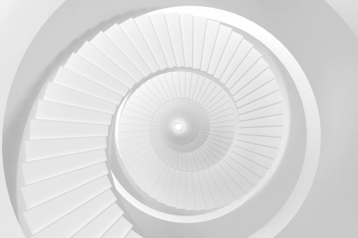 Abstract empty architecture indoor space with a spiral staircase going down, brighty lit white color. Geometric shapes and stairs arrayed in a tunnel like space. Modern design with no people.