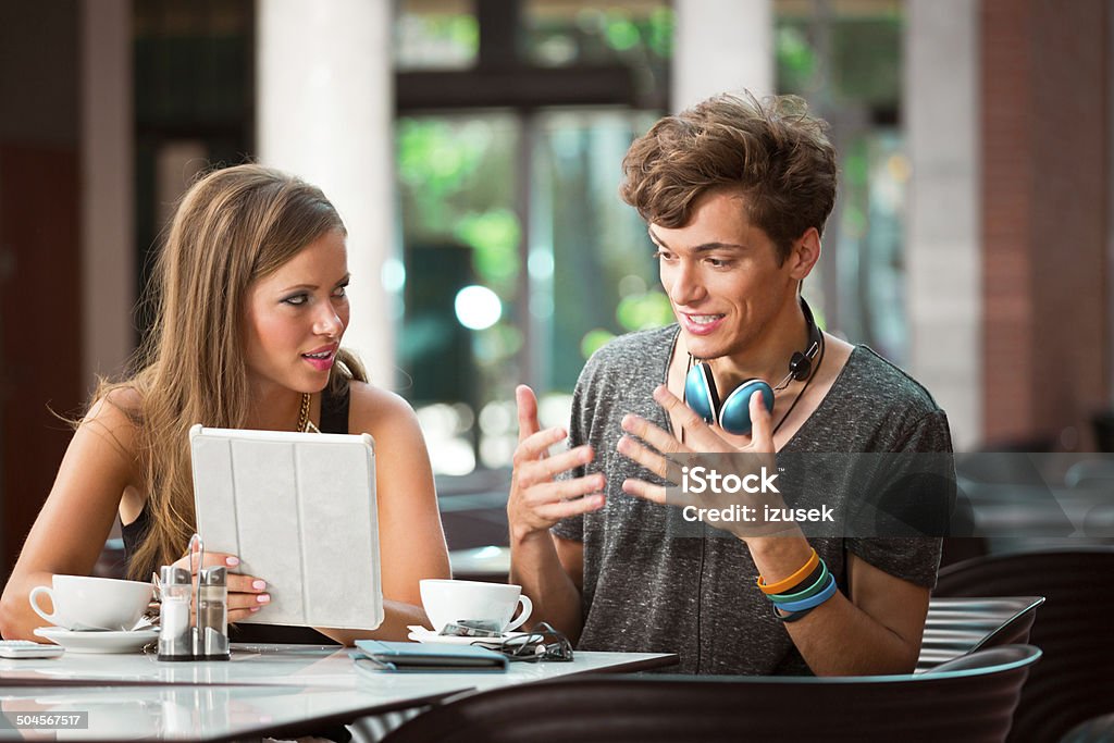 Young couple in cafe Young couple sitting in cafe, talking and using a digital tablet.  Adolescence Stock Photo