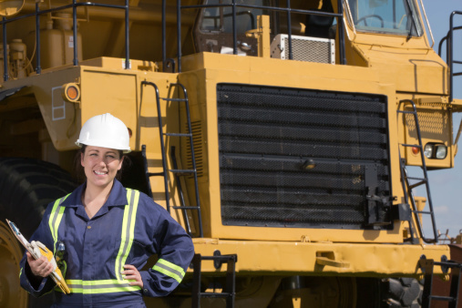 A royatly free image from the construction or oil industry of a female construction worker standing in front of a hauling truck.
