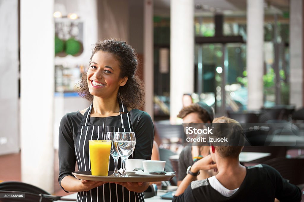 Cheerful waiter serving drinks Focus on cheerful young female waiter serving drinks with people sitting in the cafe in the background. Part-Time Job Stock Photo