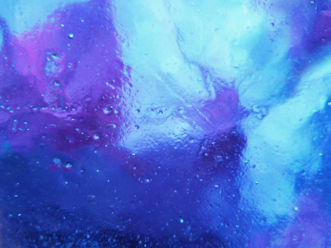 A modern abstract background image of multi colored glass with bubbles in the blue, purple, pink and turquise colored glass.