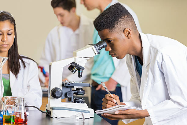 High school student taking notes while using microscope in class High school student taking notes while using microscope in class high school high school student science multi ethnic group stock pictures, royalty-free photos & images