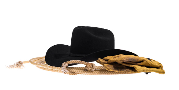 A three quarter view of a black felt Cowbot hat, showing the black leather band, the crease and the pinch on the top of the crown of the hat sitting on a lasso with a pair of old, worn, dirty leather gloves isolated on white background