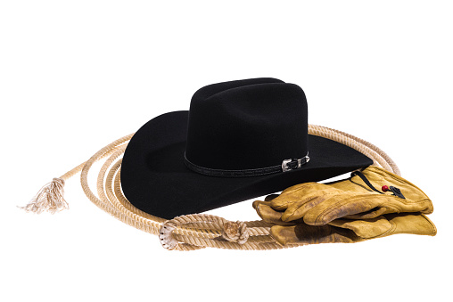 Looking down on a three quarter view  black felt Cowbot hat, showing the black leather band with a silver buckle, the crease and the pinch on the top of the crown of the hat that is sitting on a lasso and with a pair of old, worn, dirty leather gloves next to it, isolated on white background