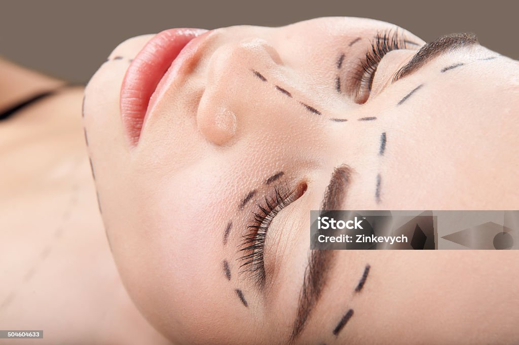 Beautiful young woman with perforation lines around her eyes and Top view portrait of beautiful young woman with perforation lines around her eyes and chin looking up before plastic surgery operation isolated on grey Adult Stock Photo