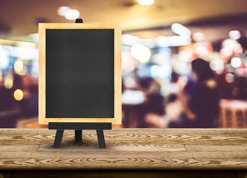 Blackboard menu with easel on wooden table with blur restaurant background, Copy space for adding your content.
