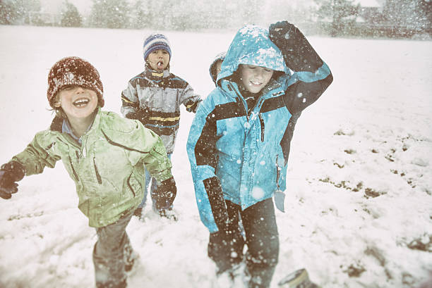 Selfie portrait of two little boys and girl in colorful clothes play outdoors during a snowfall. Active holidays with children in winter on cold days. Happy siblings having fun with snow outside.