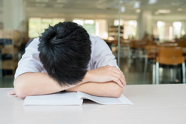 Young businessman holding his head in front of textbooks.