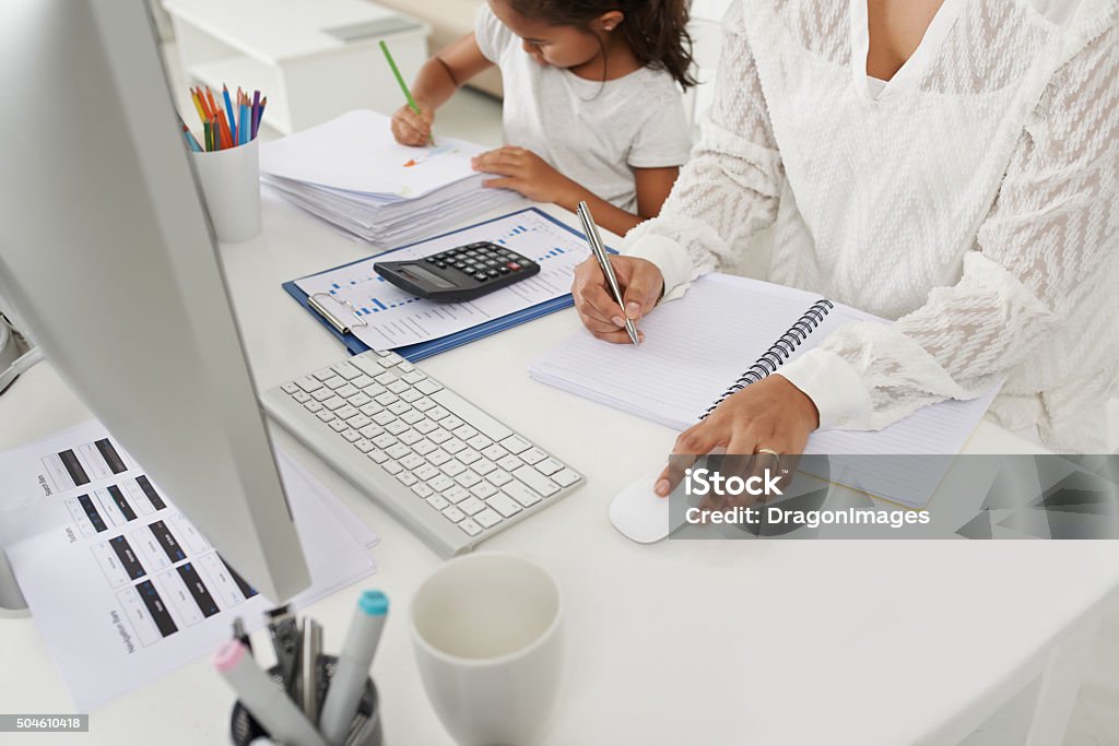 Working mother concept Business woman making notes in textbook, her daughter sitting next to her and drawing Working Mother Stock Photo