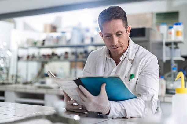 Male chemist reading medical data in laboratory. Mid adult male scientist reading scientific data in a laboratory. laboratory chemist scientist medical research stock pictures, royalty-free photos & images